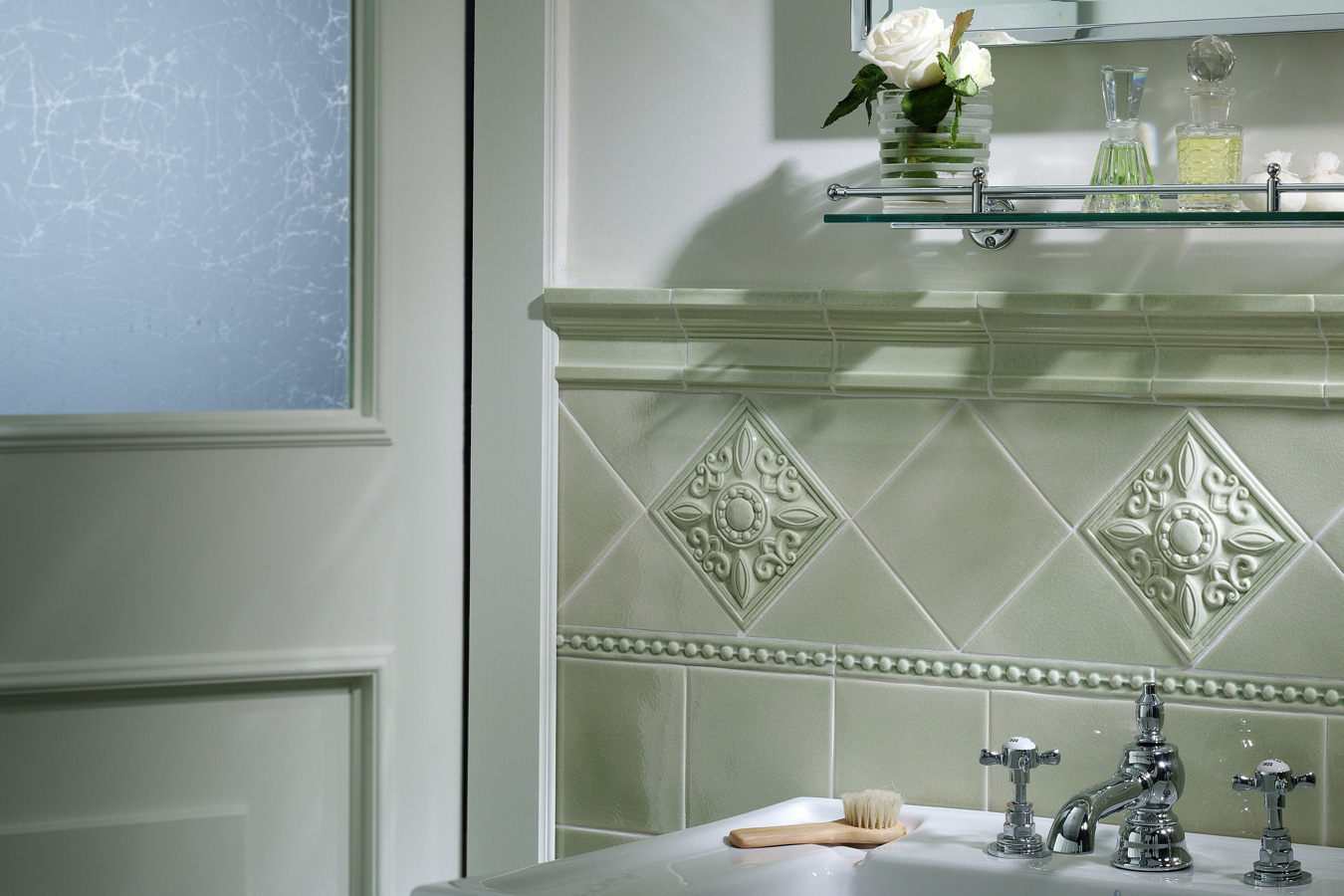 Detail koupelny s obklady Ceramiche Grazia Essenze Capitello v odstínu Magnolia s dekorativními prvky a klasickými bateriemi.